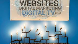 online meeting background of abstract lighting fixture made from pipe and exposed lightbulbs below graphic stating "Website Digital Marketing Digital TV" on wall