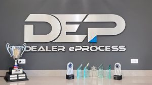 video meeting background of metallic wall logo in DEP office entrance with various industry awards on countertop underneath wall logo sign